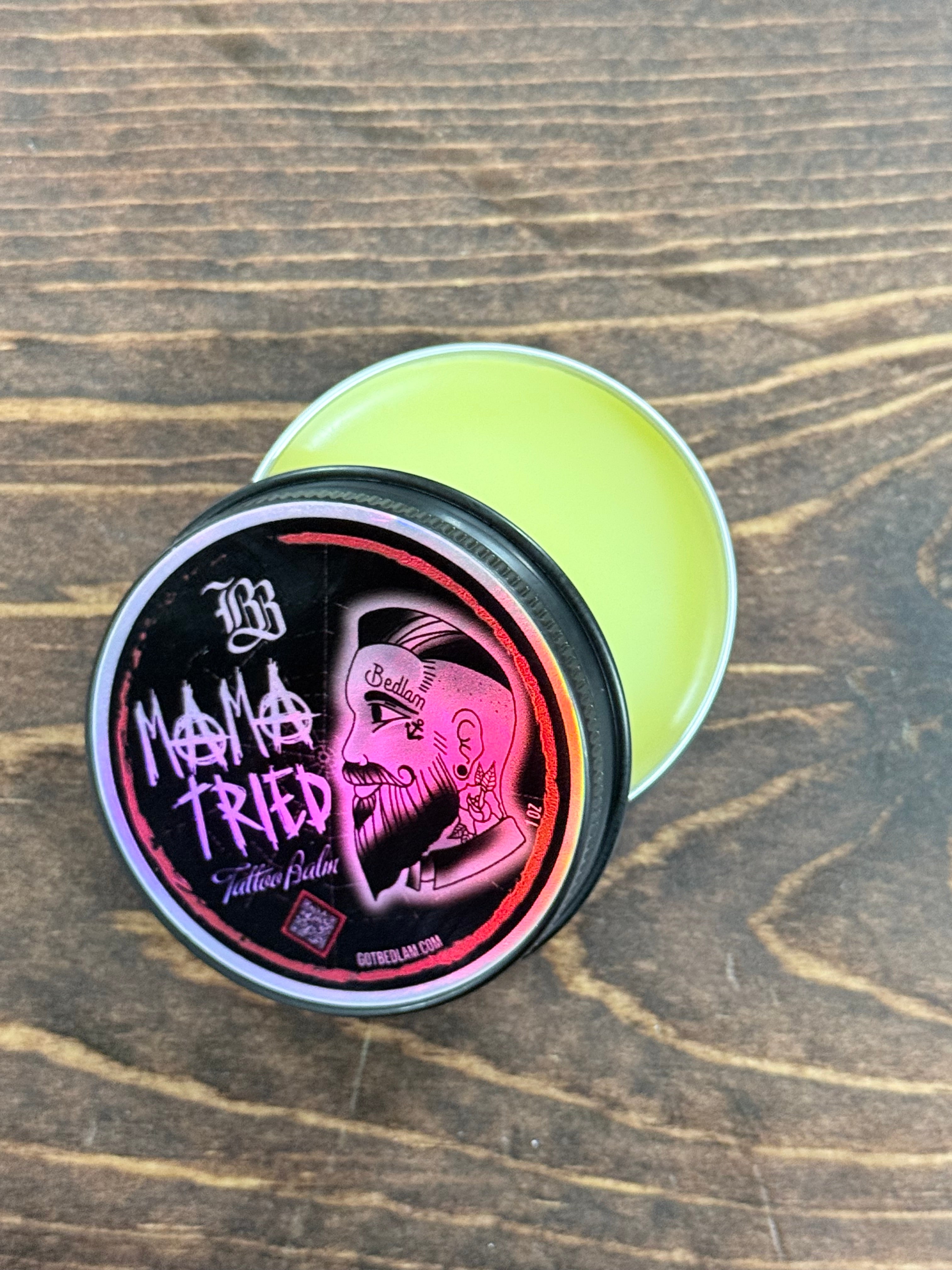 Open balm container with a holographic black and red label on a wooden surface