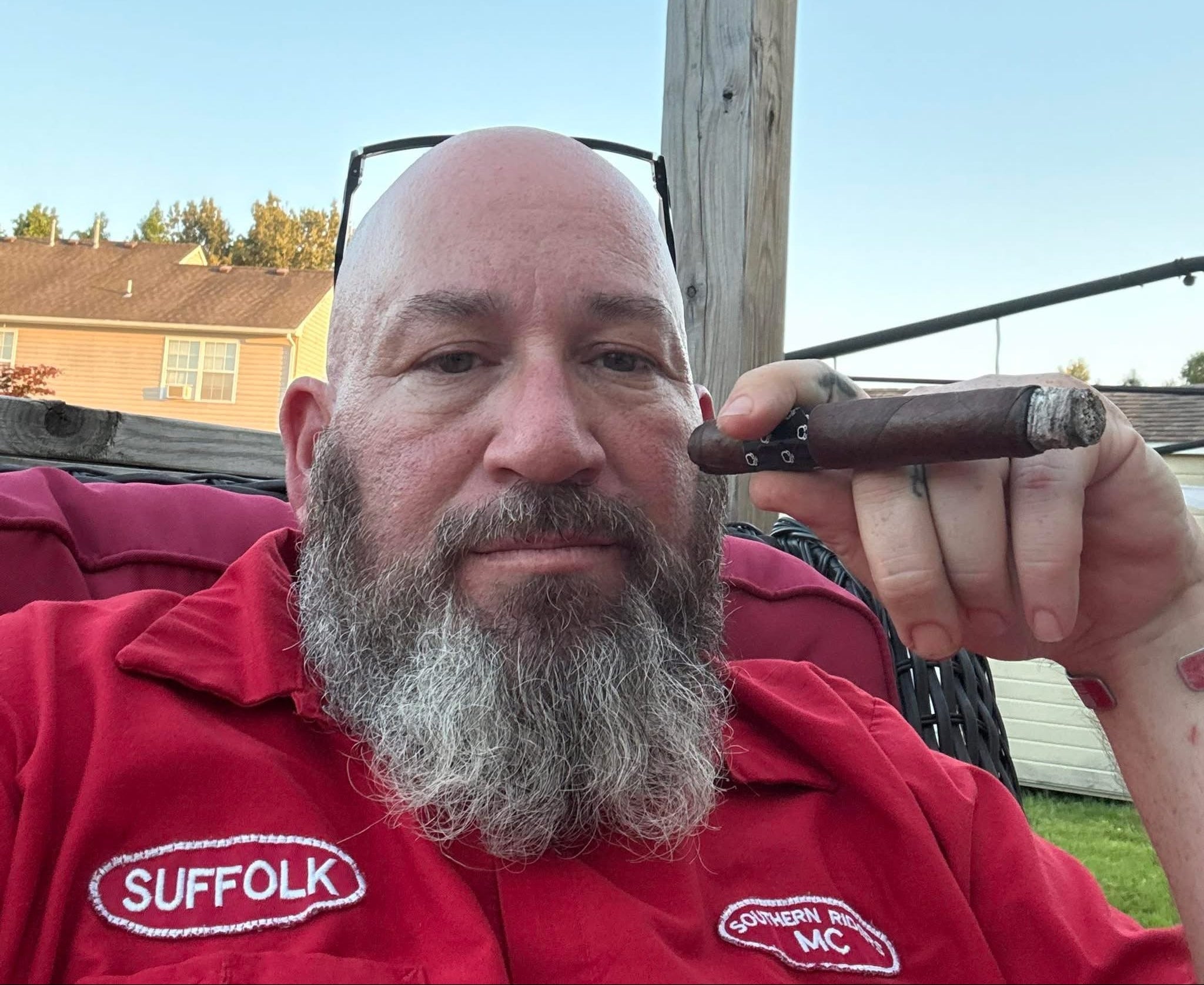 Man in a red shirt holding a cigar outdoors with a clear sky background